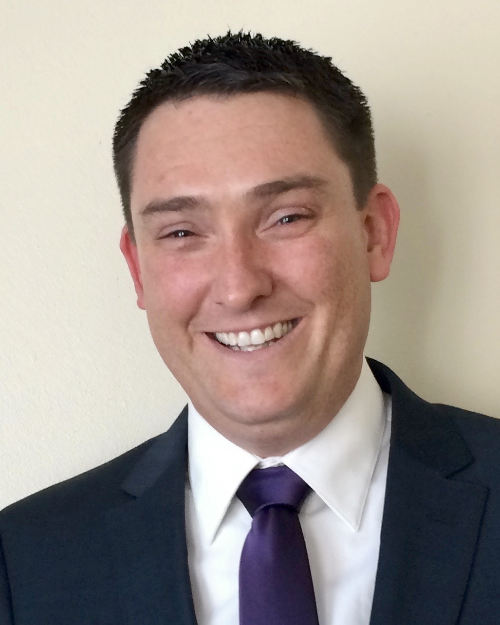 Smiling photo of Jake Simmens in a suit and purple tie